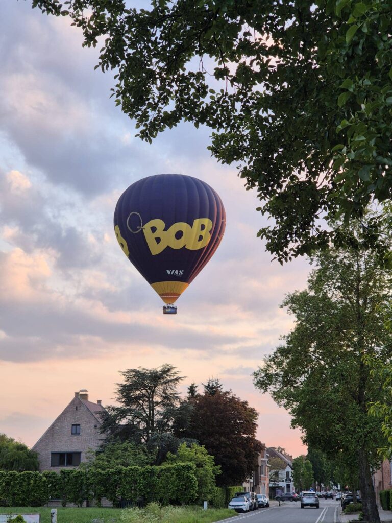 BOB luchtballon van Filva Ballonvaarten vliegt tijdens een avondballonvaart boven huizen en straat in Vlaanderen